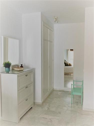 a white bedroom with a dresser and a blue chair at El Envero Apartamento in Jerez de la Frontera