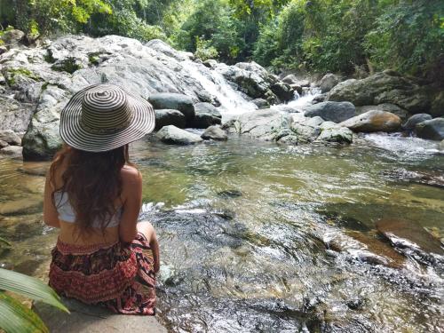 a woman in a hat sitting in front of a river at Serrano Glamping in El Zaino