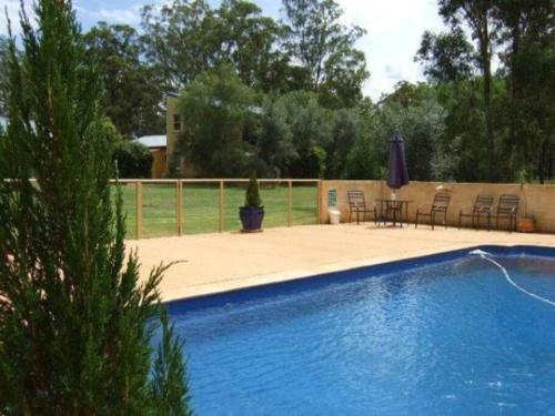 una piscina blu con sedie, tavolo e ombrellone di Chez Vous French Farmhouse Villa 4 a Pokolbin