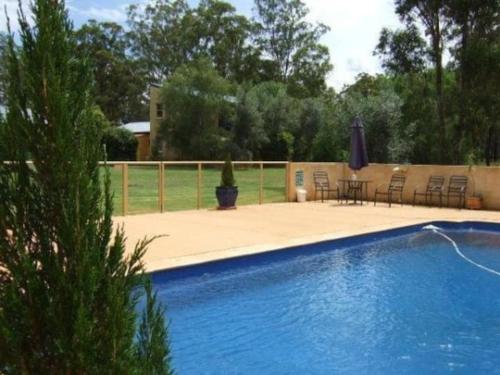a swimming pool with chairs and a table and umbrella at Chez Vous French Cottage - Pokolbin Hunter Valley! in Pokolbin