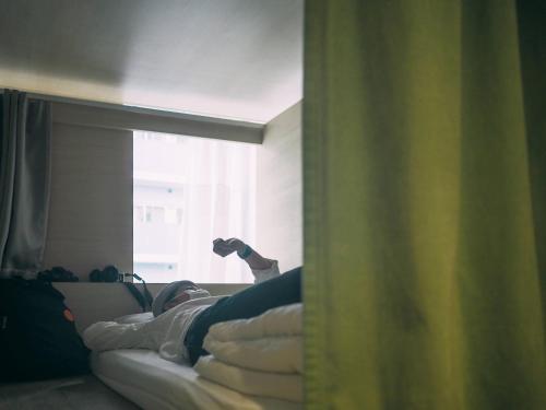 a person laying on a bed looking out a window at UNPLAN Kagurazaka in Tokyo
