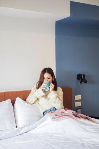 a woman sitting on a bed drinking a cup of coffee at Saffron Hill Minburi in Min Buri