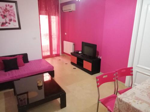 a living room with pink walls and a couch and a tv at résidence les jardins in El Aouina