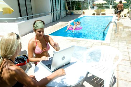 un groupe de personnes assises à une table avec un ordinateur portable au bord de la piscine dans l'établissement Esperides, à Kos