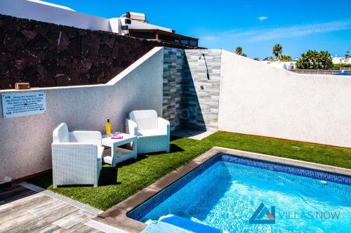 een zwembad met stoelen en een tafel naast een gebouw bij Villa Graciosa By Villas Now Ltd in Playa Blanca
