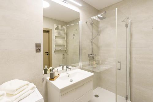 y baño blanco con lavabo y ducha. en Apartamenty Fenomen - Premium Park & Sea, Nadmorskie Tarasy FREE PARKING, SWIMMING POOL, SAUNA AND OTHER!, en Kołobrzeg