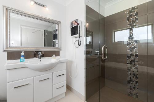 a white bathroom with a sink and a shower at Sunny on Sunlea - Mangawhai Village Holiday Unit in Mangawhai