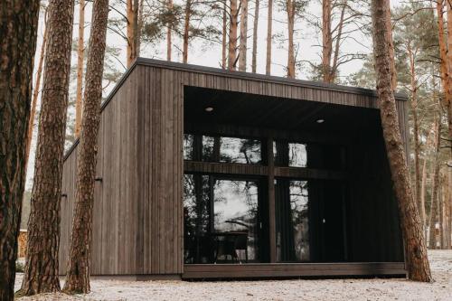 a black building with glass doors in a forest at GaujaUpe in Gauja