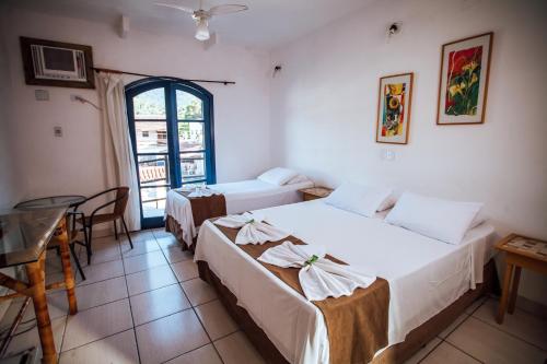 a room with two beds and a table and a window at Pousada Rafimar in Ilhabela