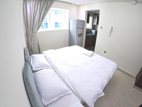 a room with a bed with white sheets and a refrigerator at Barsha Star Residence - Home Stay in Dubai