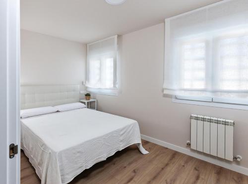 a white bedroom with a bed and two windows at A Tu Lado VUT 09306 in Burgos