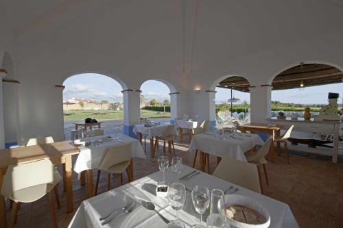 a restaurant with white tables and chairs and windows at Herdade Do Touril in Zambujeira do Mar