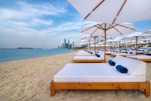 a row of beach chairs with umbrellas on a beach at Radisson Blu Hotel & Resort, Abu Dhabi Corniche in Abu Dhabi
