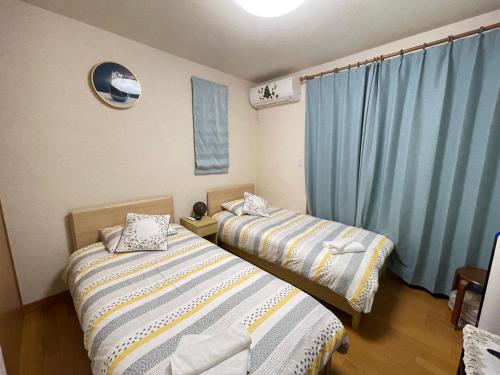 2 camas en una habitación con cortinas azules en MIKOTO HOUSE en Kashū