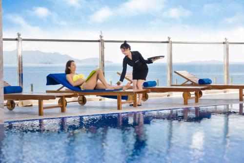 a man and woman sitting on benches next to a swimming pool at Xavia Hotel in Nha Trang