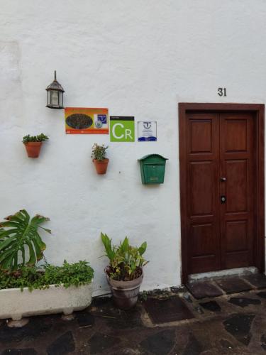 een wit gebouw met een bruine deur en een aantal planten bij La Casa del Orobal in Agaete