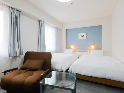 a hotel room with two beds and a couch and a glass table at Hotel Wing International Miyakonojo in Miyakonozyō