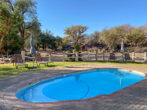 a swimming pool with two chairs and an umbrella at Ondundu Lodge in Kamanjab