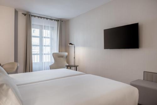 a bedroom with a white bed and a television on a wall at NH Collection Salamanca Palacio de Castellanos in Salamanca