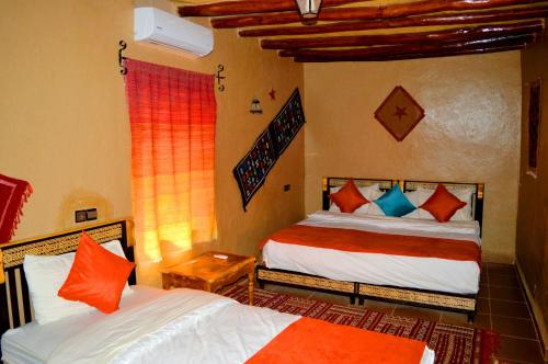 um quarto com 2 camas com almofadas laranja e azul em Auberge Les Roches em Merzouga