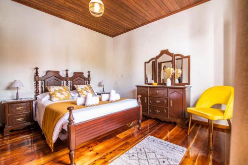 a bedroom with a bed and a yellow chair at Casa do Pinheiro with shared swimming pool in São Vicente Ferreira