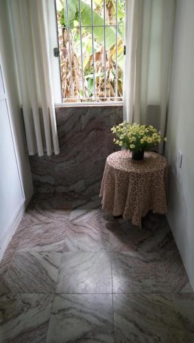 a room with a table and a window with a vase of flowers at Pousada Regina in Cachoeiro de Itapemirim
