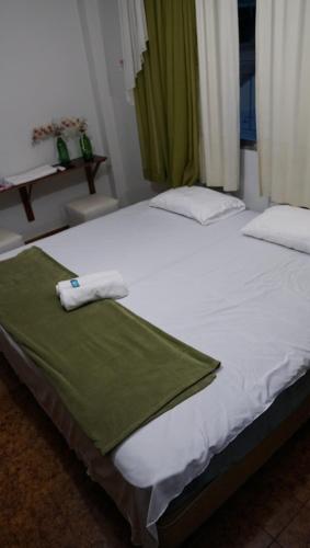 a bed with white sheets and a green blanket on it at Pousada Regina in Cachoeiro de Itapemirim