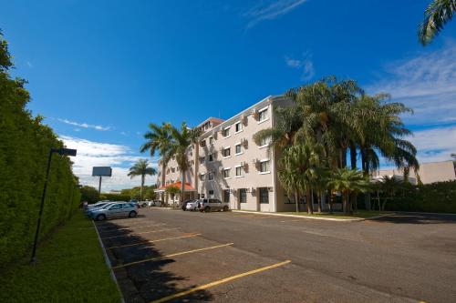a building on a street with palm trees and a car at Fênix Hotel Limeira in Limeira