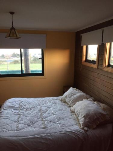 a bedroom with a white bed with two windows at CASAS Y CABAÑAS CUMBRES DEL SOL in Castro