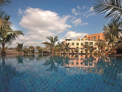 a large swimming pool with palm trees and a building at Shangri-La Qaryat Al Beri, Abu Dhabi in Abu Dhabi