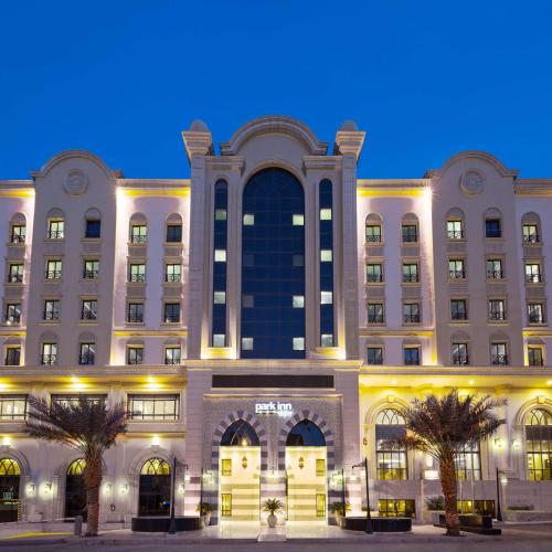 a large white building with palm trees in front of it at Park Inn by Radisson Makkah Al Naseem in Makkah