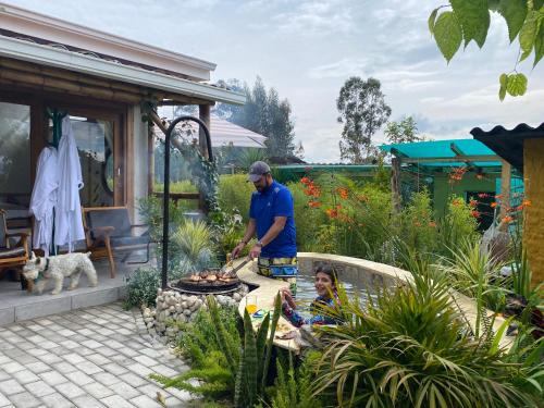 a man cooking on a grill in a garden at Hostería Colibri Aeropuerto in Tababela