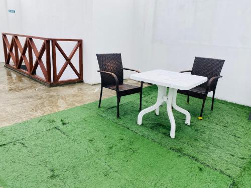 une table blanche et deux chaises sur un tapis vert dans l'établissement Pelican Beach Maafushi, à Maafushi