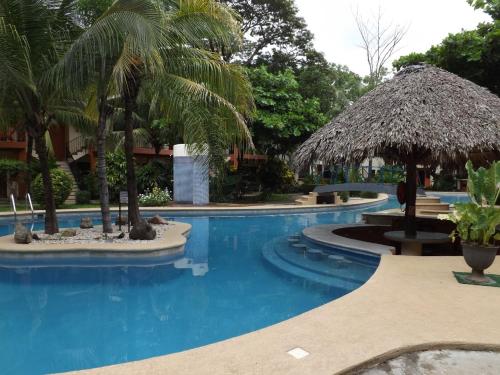 una piscina con un ombrellone di paglia e palme di Room in Condo - Nice condo to vacation in Playas del Coco a Coco