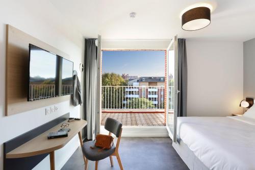 Un dormitorio con una cama y un escritorio y un balcón. en Appart Hotel Odalys City Toulouse Centre Compans Caffarelli, en Toulouse