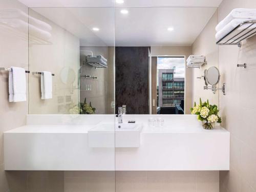 Baño blanco con lavabo y espejo en Novotel Geelong en Geelong