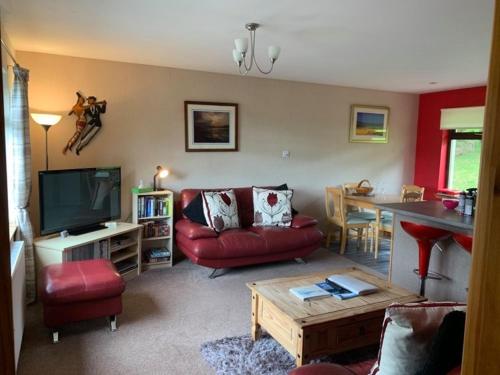 a living room with a red couch and a tv at Snowberry Cottages No1 in Onich