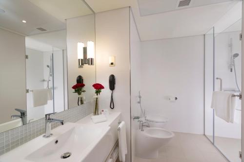 a white bathroom with a sink and a toilet at Adagio Abu Dhabi Al Bustan in Abu Dhabi