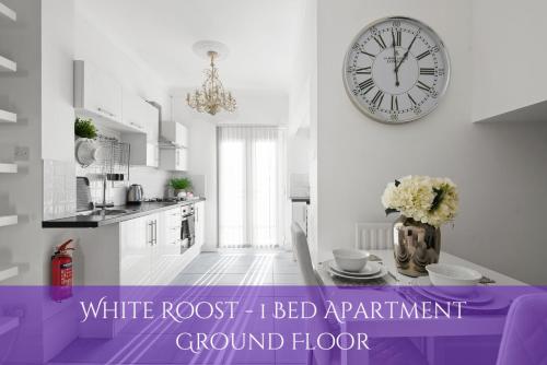 a white room with a table with a clock on the wall at The Roost Group - Stylish Apartments in Gravesend