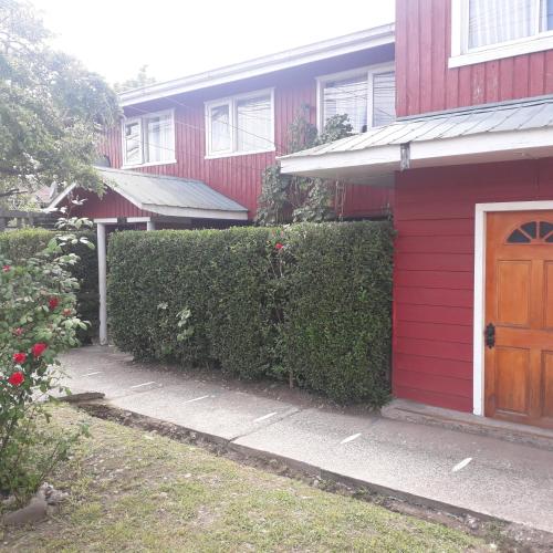 a red house with a wooden door and a hedge at Hostal Rayen in Villarrica