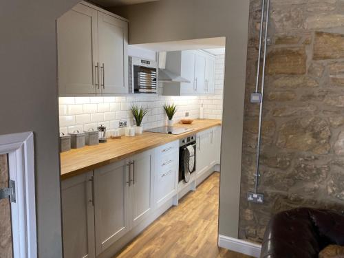 a kitchen with white cabinets and a stone wall at The Wynd Cottage in Amble