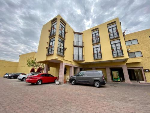 a yellow building with cars parked in a parking lot at Hotel Senorial in Querétaro