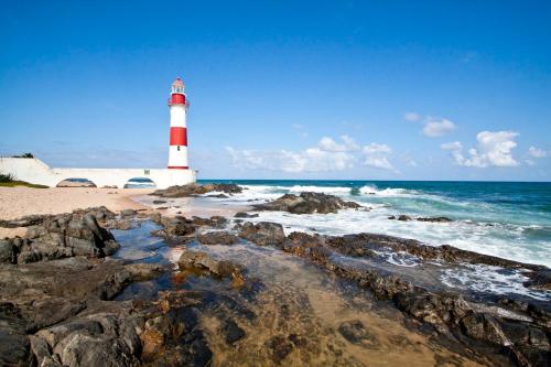 a red and white lighthouse on a rocky beach at Kitnets com AR Condicionado na Praia in Salvador