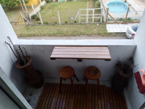 un banco y dos taburetes en un porche con ventana en Linda kitnet perto do mar!, en Tramandaí