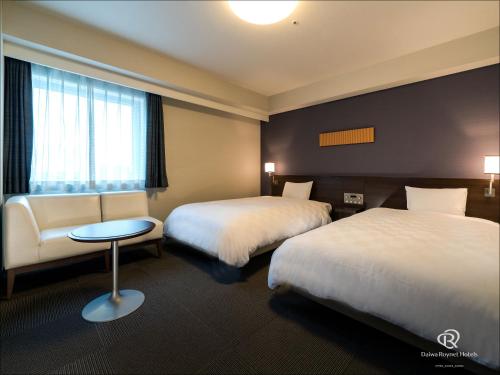 a hotel room with two beds and a table and a window at Daiwa Roynet Hotel Tsukuba in Tsukuba