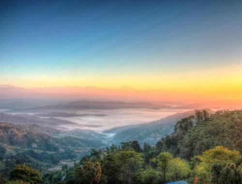 a view of a foggy valley with the sun setting at Mount Princess Hotel in Dhulikhel