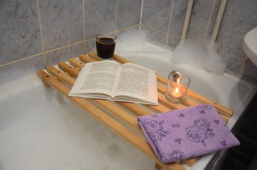 a book and a candle on a wooden tray in a bath tub at Видовая квартира на 18 этаже in Irkutsk