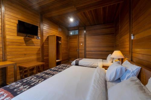 two beds in a room with wooden walls and a tv at Casa Kandara in Waingapu