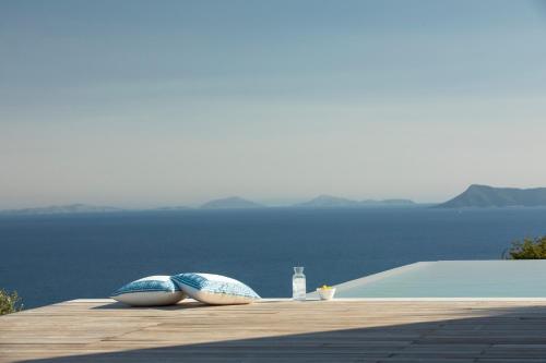 Blooms of Sivota Bay - Luxury villas with private heated pool في سيفوتا: وسادتين جالستين على سطح خشبي مع الماء