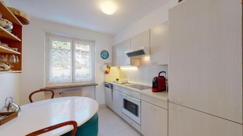 uma cozinha com armários brancos, uma mesa e uma janela em Plattas 9 em St. Moritz